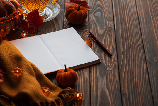 Cozy autumn scene with open notebook, warm drink, pumpkins, and fairy lights on wooden table