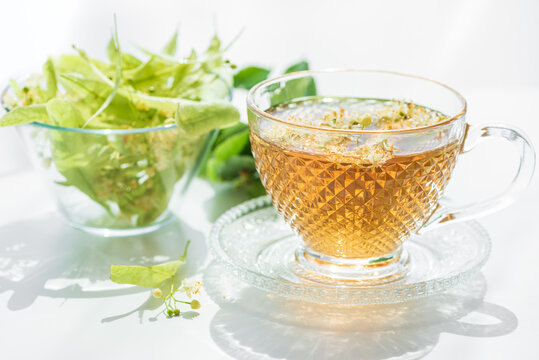 Hot cup of herbal tea made from linden flowers next to fresh linden blossoms in glass bowl