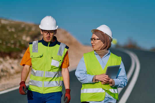 Construction Engineers Discuss Road Project While Walking on Highway Wearing Safety Gear