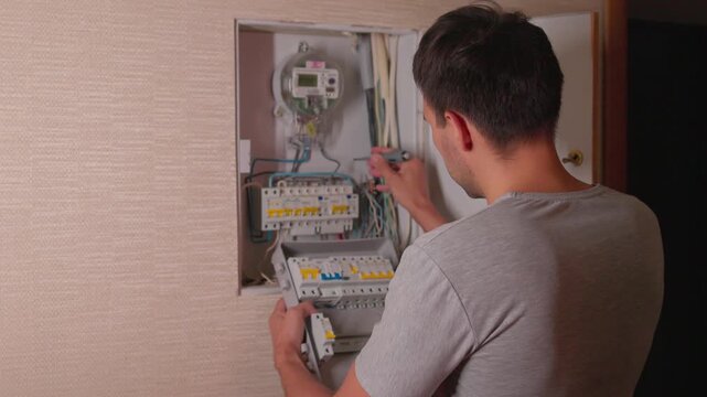 Technician removing lower circuit breaker module from open residential electrical panel, inspecting internal wiring and meter display during home safety service