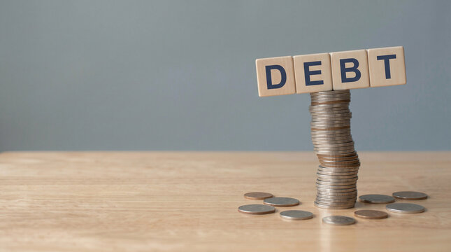 Wooden cubes DEBT on tall unstable coin stack, financial risk concept