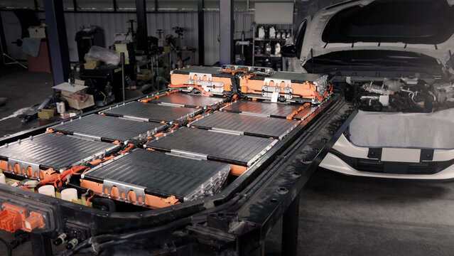 EV car service. Electric vehicle battery pack being serviced or inspected in automotive workshop. Large battery modules and high voltage components. Modern EV power systems. Lithium ion NMC NCA or LFP