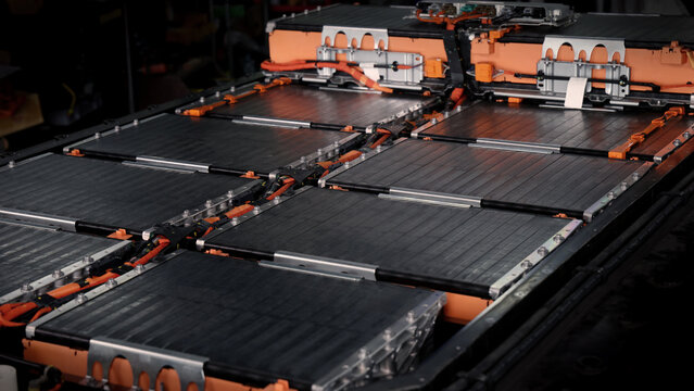 EV car service. Electric vehicle battery pack being serviced or inspected in automotive workshop. Large battery modules and high voltage components. Modern EV power systems. Lithium ion NMC NCA or LFP