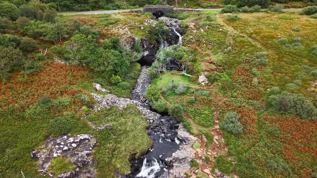 Eas Fors waterfall cascading down dark basalt cliffs into a rocky pool on the Isle of Mull, Scotland, green moorland surrounding the stream