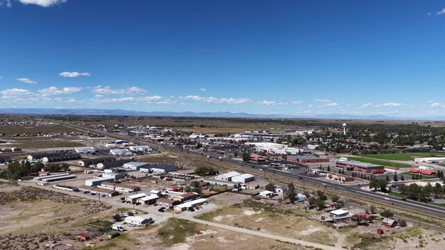 Wide aerial of commercial corridor along highway 285 in Alamosa Colorado with mountains in the distance under a blue sky with clouds