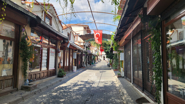 Historic Muğla Arasta Bazaar in Menteşe, featuring cobblestone streets, traditional wooden shops, vine trellises, and a Turkish flag, preserving the atmosphere of Ottoman-