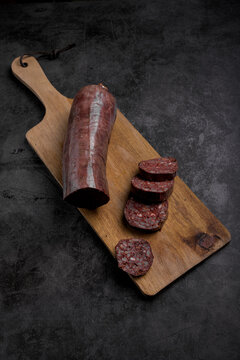 Sliced Spanish morcilla blood sausage on wooden board with parsley garnish over dark slate background, rustic traditional food overhead view