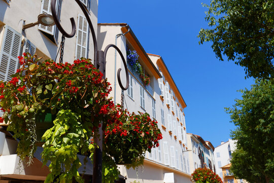 Hanging baskets of red begonias on a wrought-iron bracket against a French townhouse in Antibes, French Riviera, , France