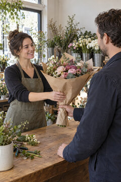 Fleuriste remettant un bouquet &agrave; un client au comptoir de sa boutique