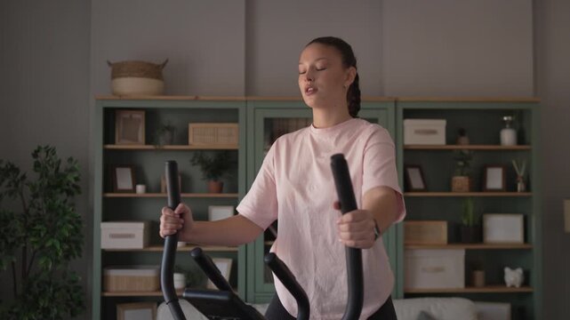 Young woman training on elliptical machine at home