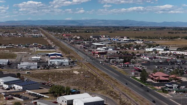 Aerial of commercial buildings and highway 285 with railroad tracks in Alamosa Colorado under a cloudy sky with mountains in the distance