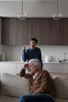 Angry senior wife arguing and emotionally gesturing at older husband during family conflict at home, irritated exhausted woman shouting at ignorant aged man on couch, disagreement and marriage crisis.