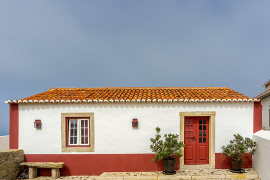 Traditional Portuguese house in Azenhas do Mar featuring white plastered walls, a vibrant red door, a single window, and a classic terracotta tiled roof against a clear sky