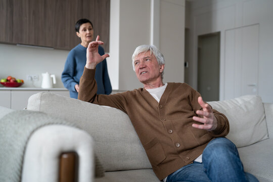 Annoyed elderly husband arguing with irritated wife, senior married couple in relationship crisis, distressed man emotionally gesturing and speaking with frustrated older woman, heated home argument.