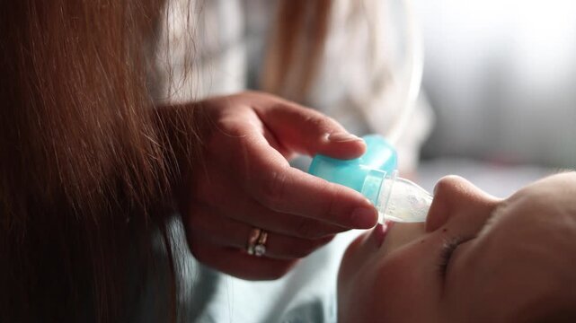 Extreme close up of calm baby lying still while mother clears nasal mucus with aspirator. Slow motion footage captures trust during routine infant care.