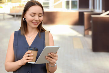Digital nomad lifestyle and remote work, young woman using tablet computer and holding coffee cup while standing in urban outdoor environment © Pixel-Shot