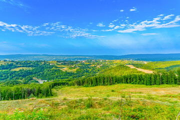 Obraz premium Panoramic view of green forested hills and valleys under bright blue sky with white clouds