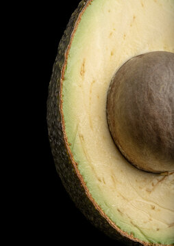 Close up of a ripe avocado half showing the textured skin and large central seed on black background