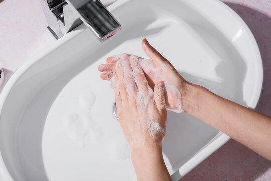 Hand hygiene and disease prevention, person washing hands with soap and water in a bathroom sink to maintain personal health and cleanliness standards