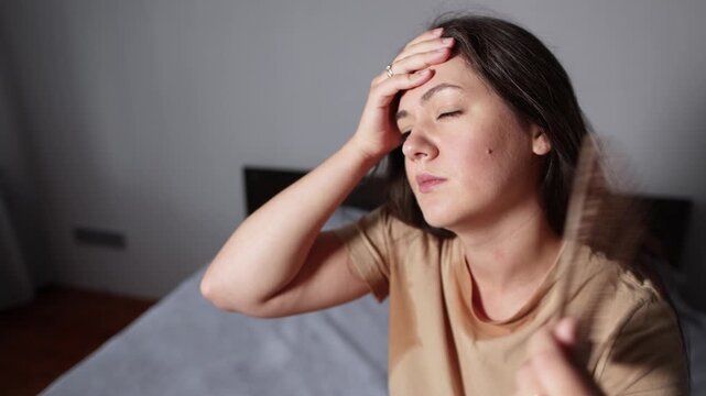 Sweaty young woman sits on bed struggling to cope with intense heat and breathlessness. Slow motion footage highlights fatigue during extreme summer weather.