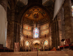 Interior view of cathedral apse decorated with religious frescoes, golden mosaics, and stained glass window in Strasbourg © virin
