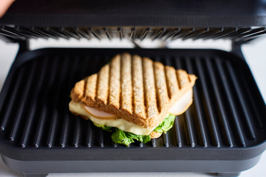 Grilled sandwich with cheese, lettuce and sliced meat cooking in open sandwich press