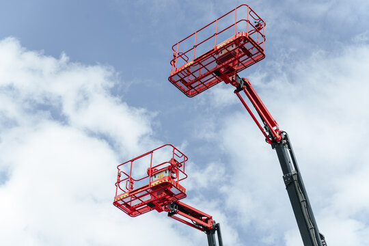 Red Aerial Lifts Extend High Into The Cloudy Sky. Industrial Equipment Awaits Maintenance Tasks