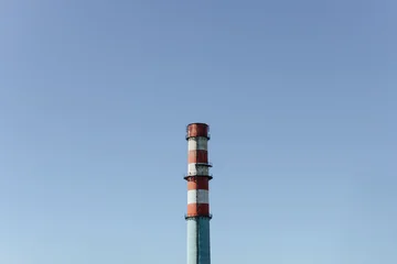 Tall Industrial Chimney Rises Against Clear Blue Sky. Striped Smokestack Marks Factory Infrastructure. © vladdeep
