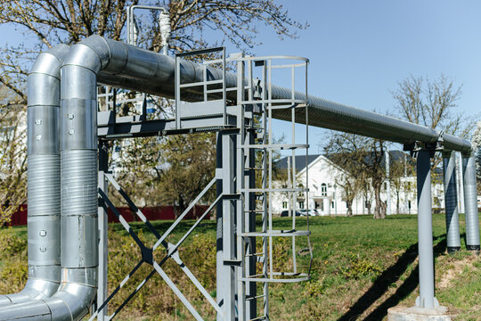Insulated Industrial Pipes Curve Along Steel Support Framework. Outdoor Utility Infrastructure Stands Near Railroad Tracks