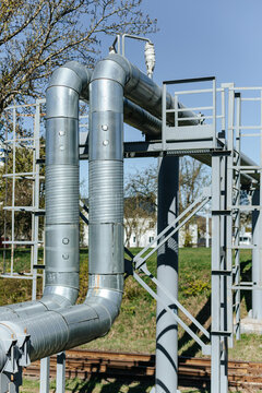 Insulated Industrial Pipes Curve Along Steel Support Framework. Outdoor Utility Infrastructure Stands Near Railroad Tracks