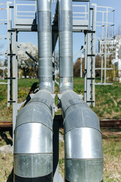 Insulated Industrial Pipes Curve Along Steel Support Framework. Outdoor Utility Infrastructure Stands Near Railroad Tracks