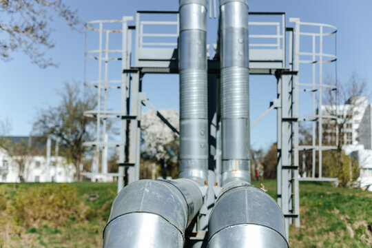 Insulated Industrial Pipes Curve Along Steel Support Framework. Outdoor Utility Infrastructure Stands Near Railroad Tracks