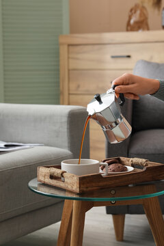Morning coffee routine and relaxation, person pouring fresh espresso from a moka pot into a cup with chocolate cookies on a wooden tray in a cozy home