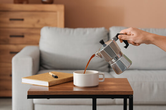 Morning routine and remote work break, person pouring fresh coffee from moka pot into cup at home office desk with notebook for productivity and focus