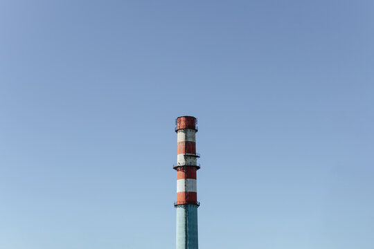 Tall Industrial Chimney Rises Against Clear Blue Sky. Striped Smokestack Marks Factory Infrastructure.