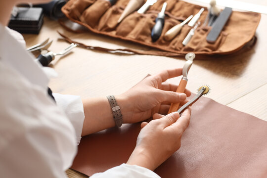 Craftsmanship and artisan leatherwork, leather crafter holding stitching tools and tracing wheels at a workshop desk for handmade goods production