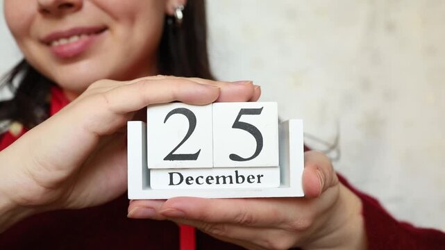 Young woman brunette in festive Christmas look keeping in hands white wooden calendar with Christmas date 25 of December close up. Christmas celebration preparation, catholic religion holiday date
