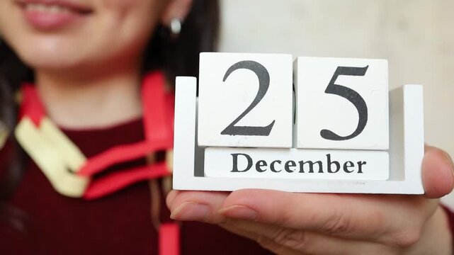 Young woman brunette in red festive Christmas look keeping in hands white wooden calendar with Christmas date 25 of December close up. Christmas celebration preparation, catholic religion holiday date
