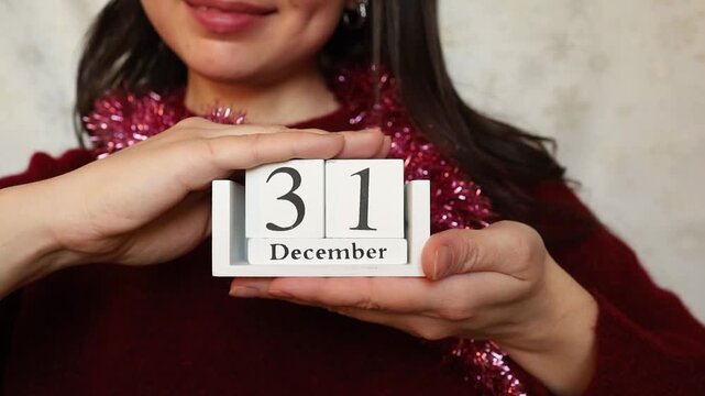 Young woman brunette in red festive look keeping in hands white wooden calendar with New year eve date 31 of December close up. Christmas and New year celebration preparation, holiday date