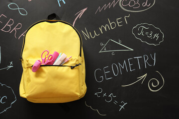Back to school education and learning, yellow backpack with stationery supplies on a blackboard with math formulas and geometry drawings for students © Pixel-Shot