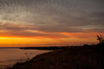 Obraz premium coastal landscape with calm sea and silhouetted wind turbines on the distant horizon at Kaliakra Cape, Bulgaria, dramatic golden orange sunset sky, grainy texture, high quality photo