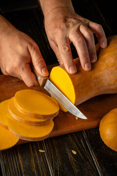 Hands are slicing smoked cheese into even rounds on wooden board. Sharp knife works through firm golden wheel, creating tidy stack with focused, homely kitchen style as cheese is portioned.