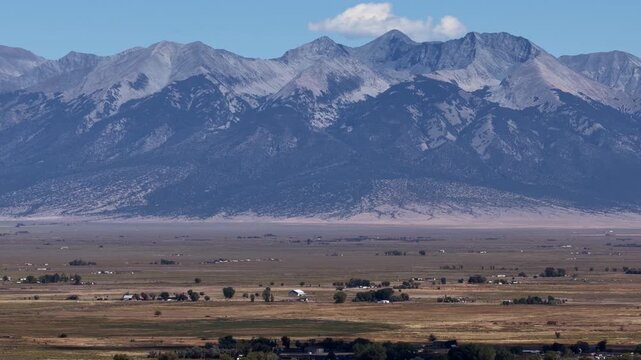 Aerial telephoto of the massive Sangre de Cristo Mountains and San Luis Valley floor featuring scattered farmhouses and trees near Alamosa Colorado