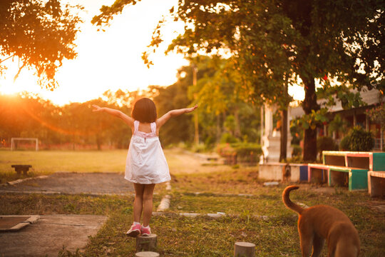 Little Girl Balancing on Wooden Stump with Arms Spread Open at Sunset Park