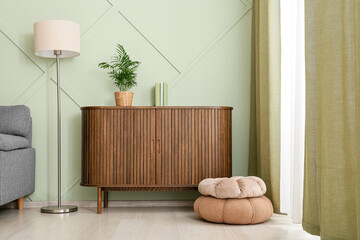 Obraz premium Interior design and home comfort, modern living room with wooden sideboard and soft cushions in a cozy apartment with sage green wall and floor lamp