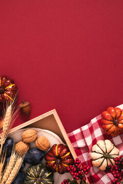 Thanksgiving Day vertical flat lay with decorative pumpkins, walnuts, plums and wheat ears on red background. Cozy autumn harvest composition with empty copy space for text, greeting or poster.