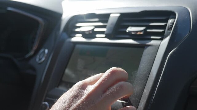 Hand touches navigation screen on car dashboard with map displayed. Concept of vehicle technology, navigation and driving