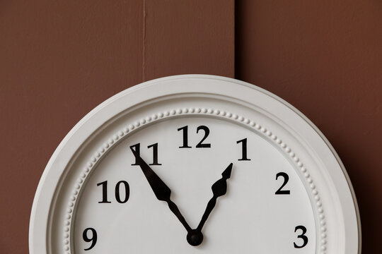 Deadline pressure and time management, white wall clock showing five minutes to one on a brown background for business planning and schedule efficiency