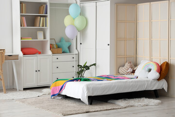Childhood celebration and birthday party concept, colorful balloons and rainbow decor in a cozy kids bedroom interior with a single bed and furniture © Pixel-Shot