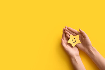 Fototapeta premium Customer satisfaction and positive feedback, hands holding a yellow star with a smiley face for service excellence and quality rating on a yellow background